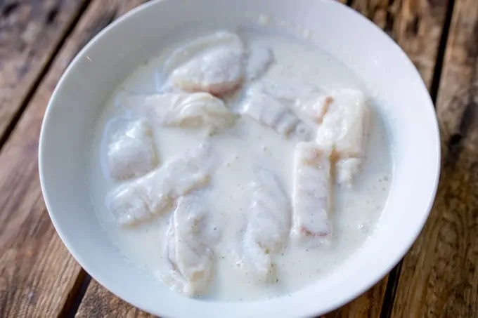 Sliced fish marinating in a bowl of buttermilk and seasoning