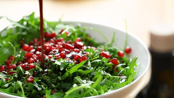 Dressing being poured over rocket leaves and pomegranate seeds