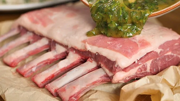 Honey mustard and herb sauce being spread on a rack of lamb