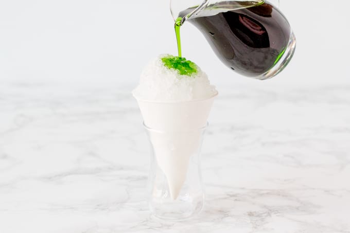 Pouring green apple syrup onto a cone of shaved ice