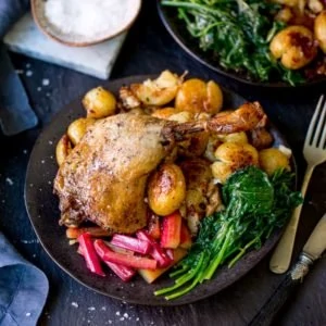 Square image of duck leg confit with roasted rhubarb, spinach and crushed roast potatoes