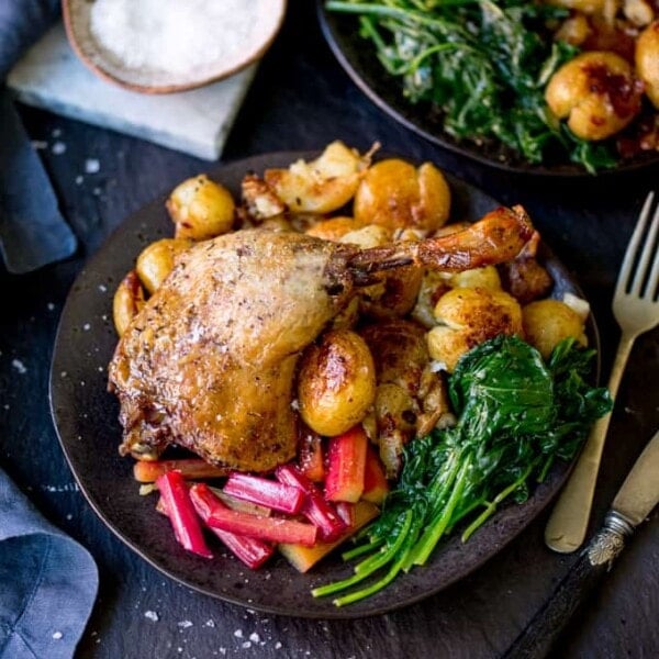 Square image of duck leg confit with roasted rhubarb, spinach and crushed roast potatoes
