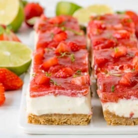 Square image of strawberry and rhubarb cheesecake bars with jelly topping and lime zest sprinkled on top
