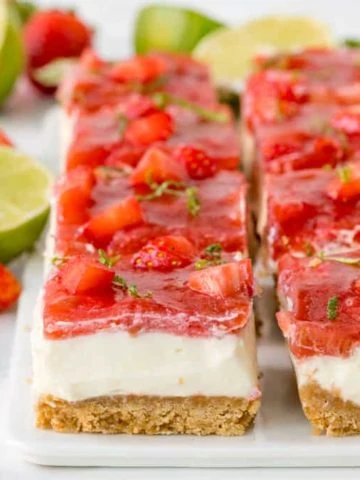 Square image of strawberry and rhubarb cheesecake bars with jelly topping and lime zest sprinkled on top