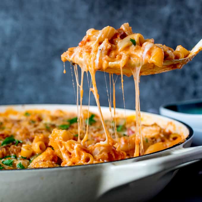 Square image of a spoonful of chicken and bacon mac and cheese being scooped out of pan. Cheese is stretching.