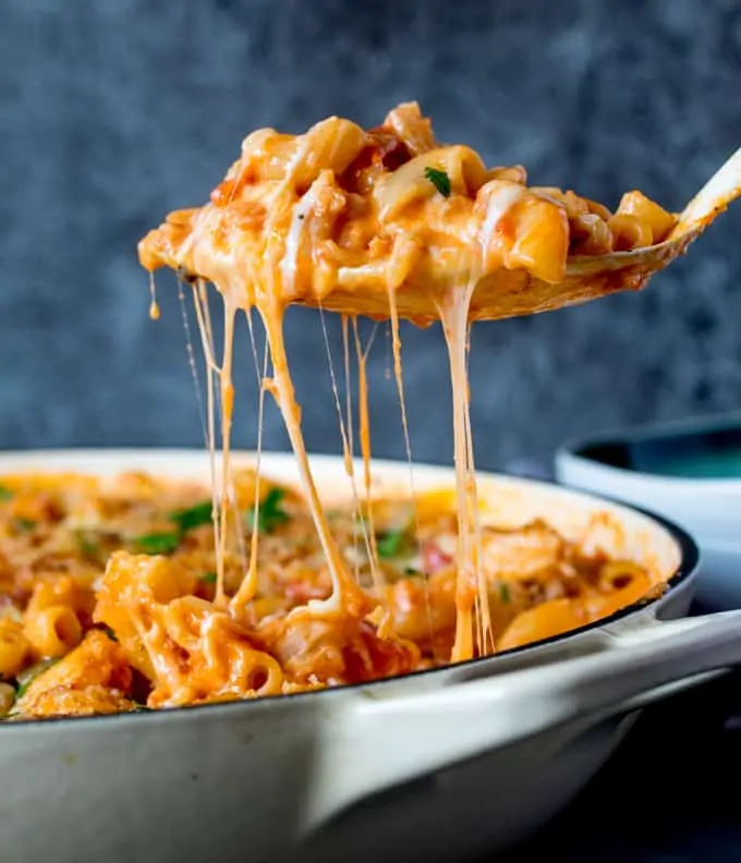 Spoonful of chicken and bacon mac and cheese being scooped out of pan. Cheese is stretching.