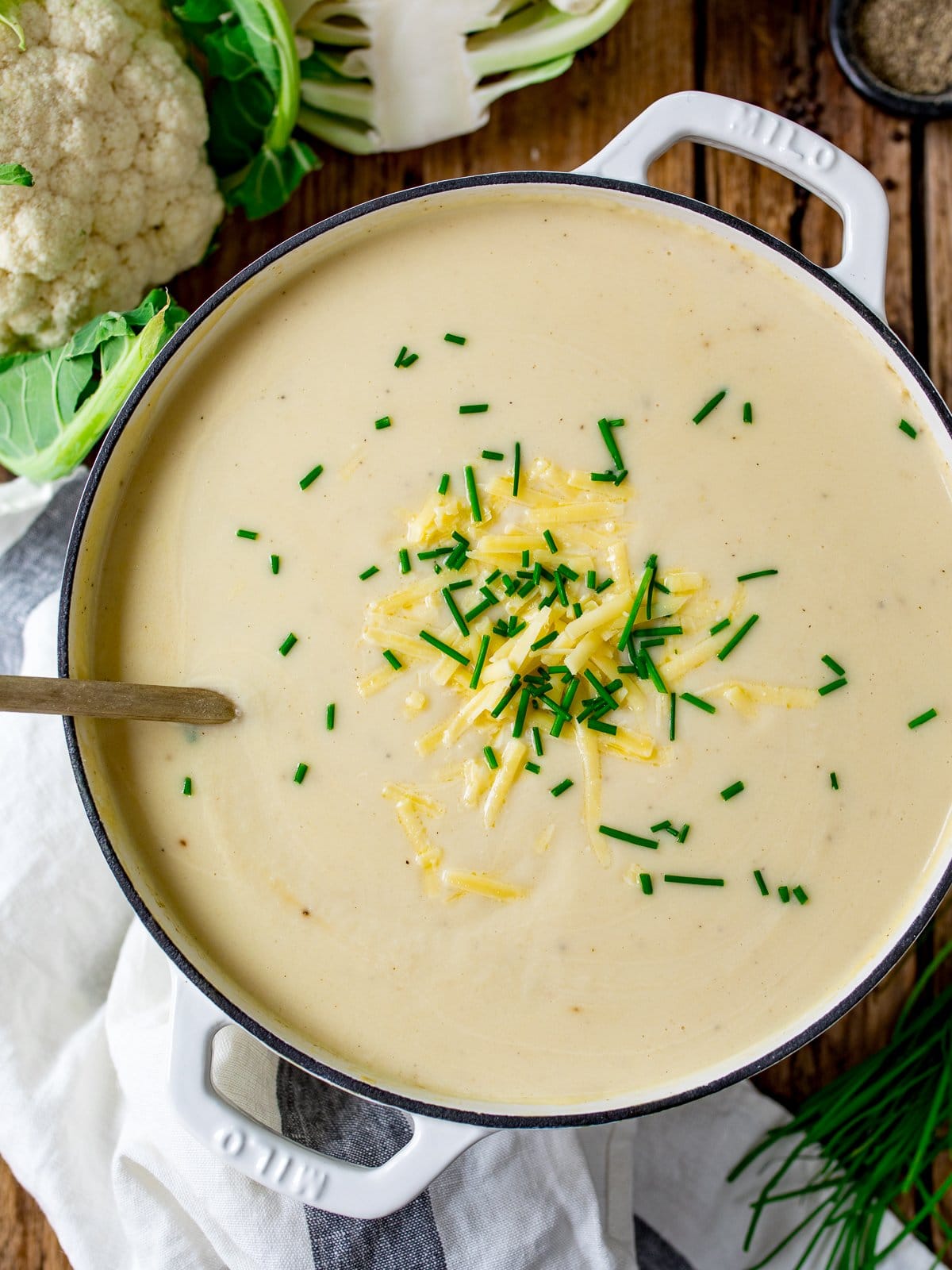 Overhead image of a large pan filled with cauliflower soup topped with grated cheese and chopped chives