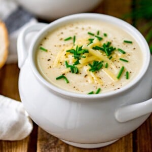 Close up of a white bowl filled with cauliflower soup and topped with chopped chives, grated cheese and black pepper