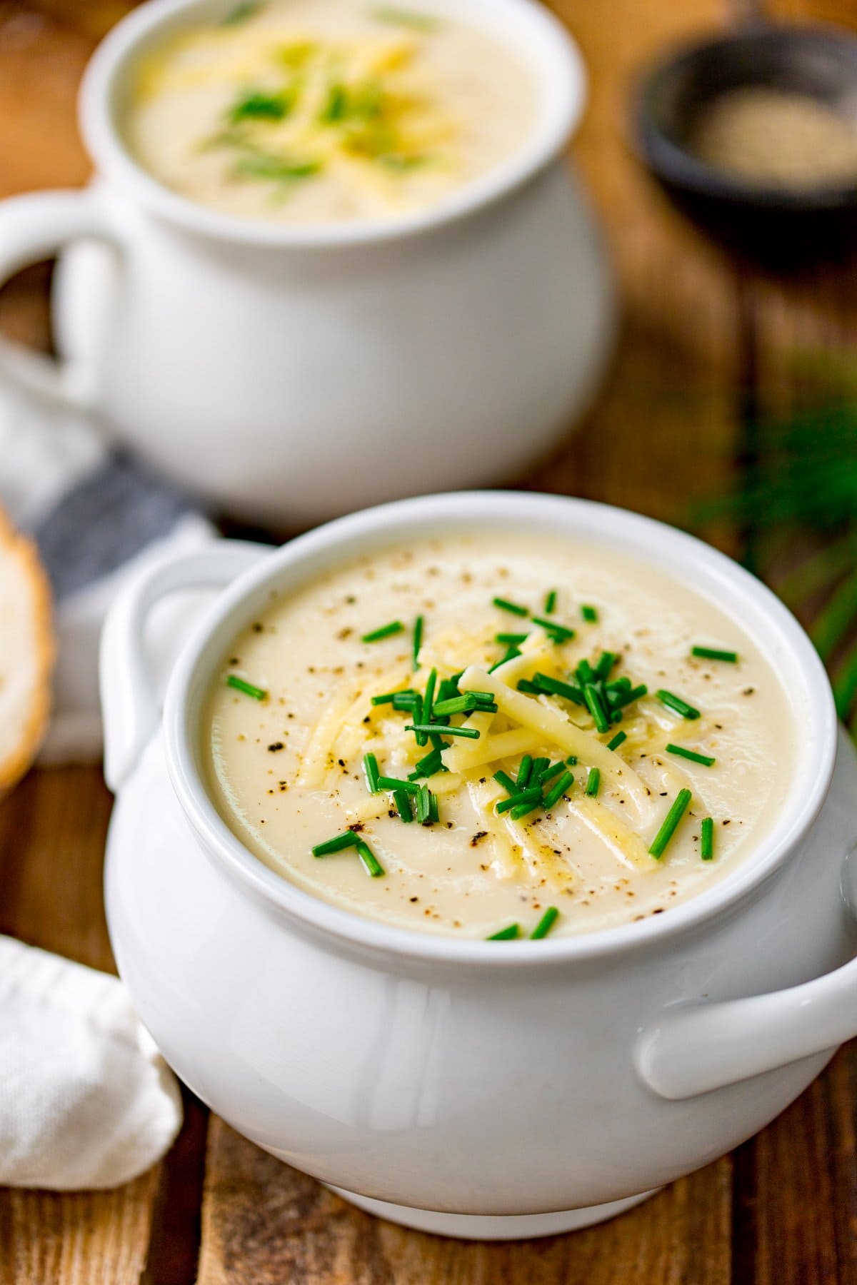 Two soup bowls filled with cauliflower soup on a wooden table. Soup is topped with chopped chives.