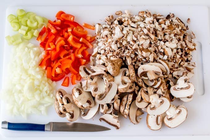 White chopping board with diced and sliced mushrooms, chopped peppers and chopped onion