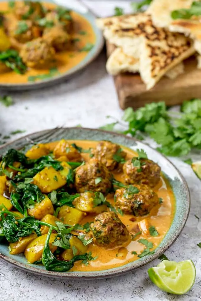 Beef Kofta with saag aloo on a plate. Cilantro and naan bread in the background