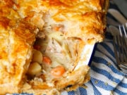 A dish of creamy chicken pie with puff pastry sat on a blue and white striped cloth.