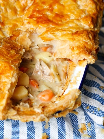 A dish of creamy chicken pie with puff pastry sat on a blue and white striped cloth.