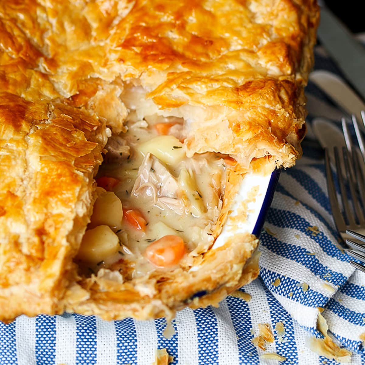 A dish of creamy chicken pie with puff pastry sat on a blue and white striped cloth.