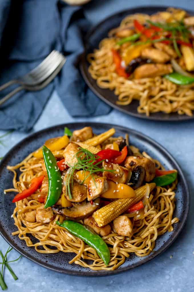 Plate of honey and soy chicken stir fry with noodles, further plate in background
