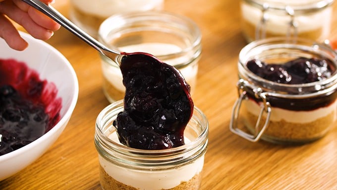 Spooning berry mixture on top of mason jar cheesecakes