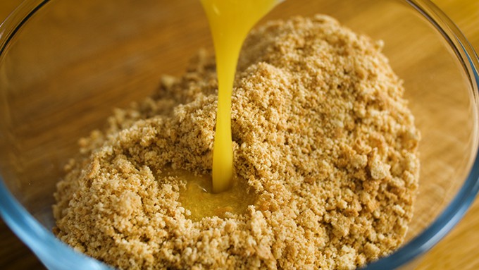 Melted butter being poured into a bowl of crushed biscuits.