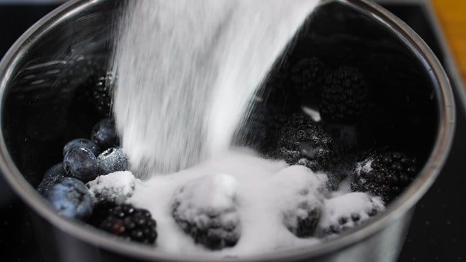 Sugar being poured into a pan with blueberries and blackberries