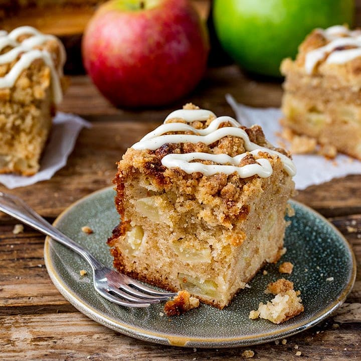 Square image of a slice of apple streusel cake with vanilla icing.