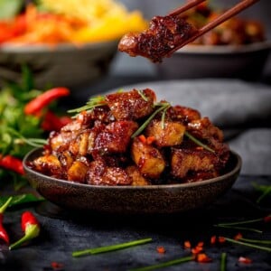 صورة مقربة لوعاء من قطع بطن لحم الخنزير الصيني اللزج.  يتم أخذ قطعة من الوعاء باستخدام زوج من عيدان تناول الطعام.