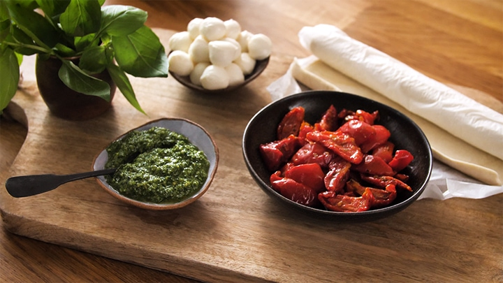 chopping board with sundried tomatoes, pesto, pastry and mozzarella