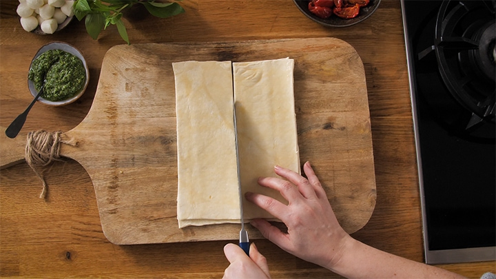 Slicing raw puff pastry into squares for caprese pastry bites