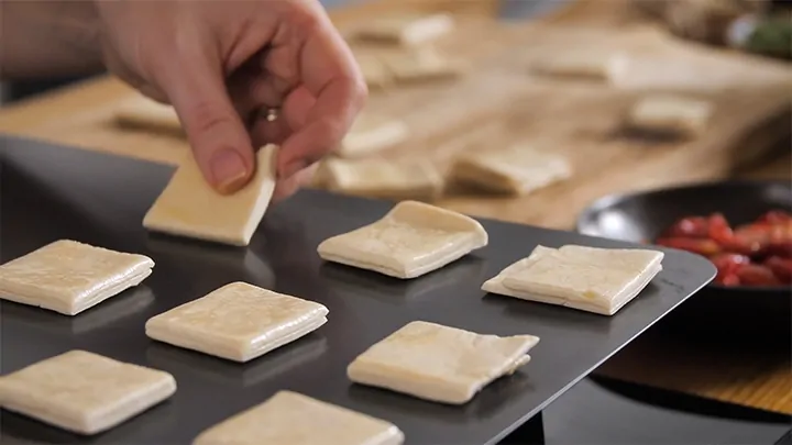 Places squares of raw pastry on a baking sheet