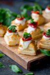 Close up of puff pastry caprese bites - with mozzarella, pesto and sundried tomato - on a serving board