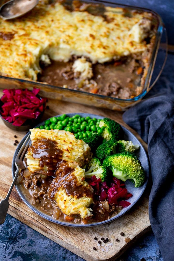 Cottage pie on a plate with gravy, broccoli, peas and red cabbage