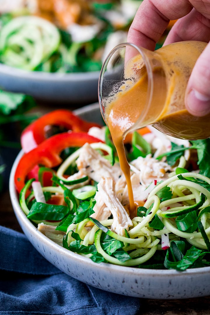 Thai peanut sauce being poured on chicken zoodle salad