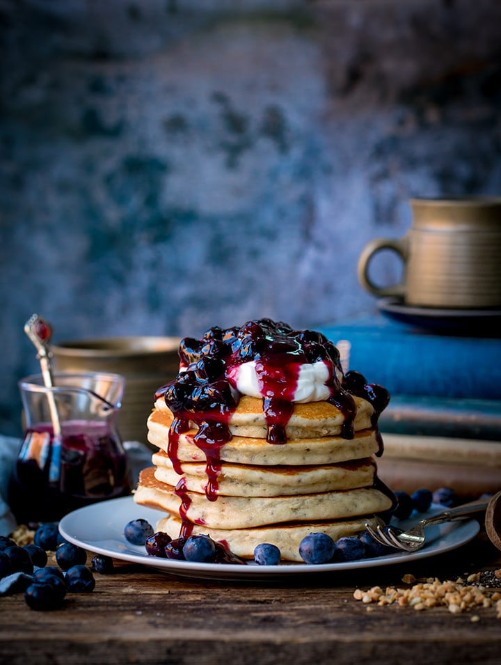 Stack of chia hazelnut pancakes on a plate with greek yogurt and blueberry compote dripping down