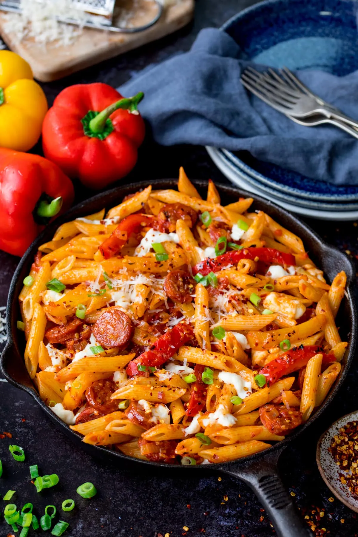 Penne arrabbiata in a pan with mozzarella and chorizo. The pan is on a dark background and there are ingredients scattered around.