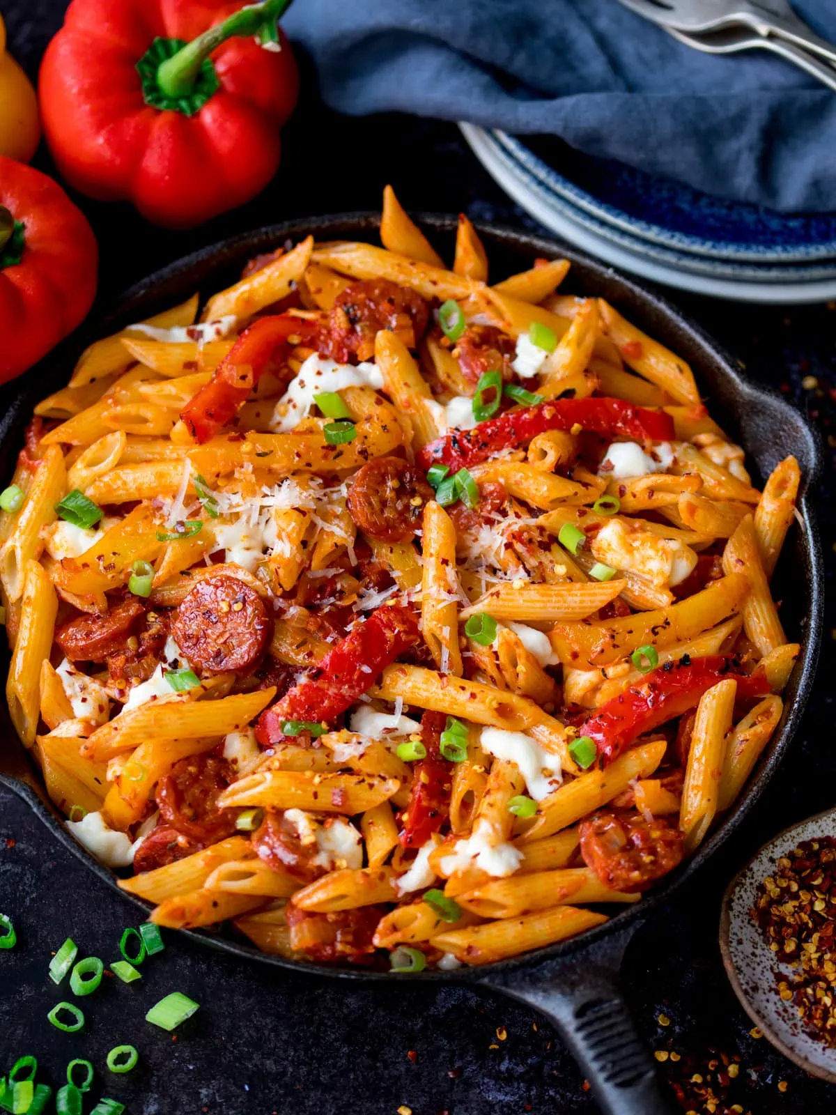 penne arrabbiata in a pan with mozzarella and chorizo. The pan is on a dark background and there are ingredients scattered around.