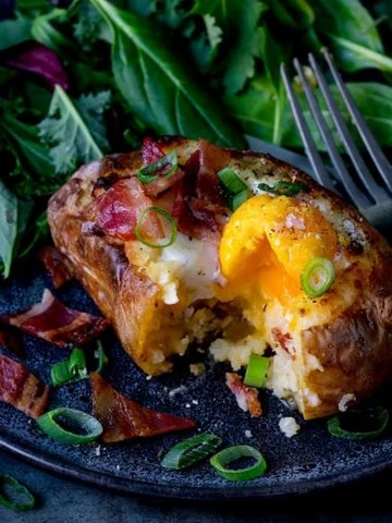 Square image of egg and bacon stuffed baked potato with runny egg on a dark plate