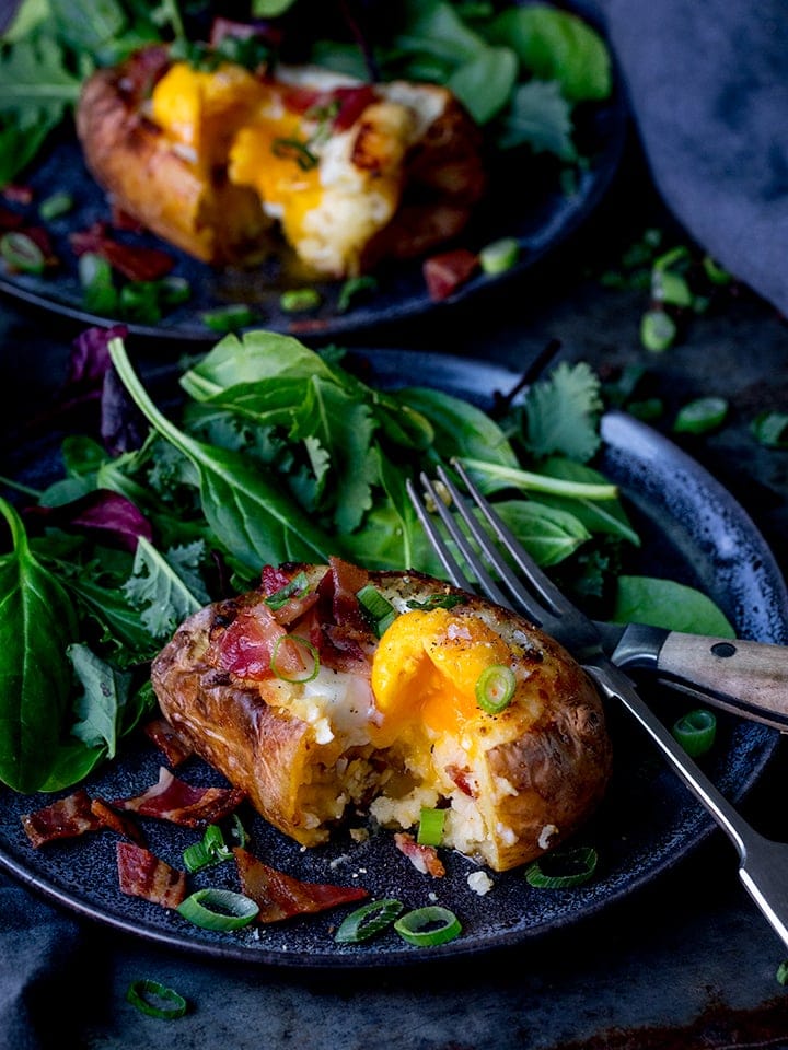 Egg and bacon stuffed baked potato with runny egg on a dark plate