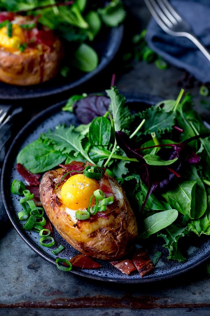 Egg stuffed baked potato on a dark plate and background with salad