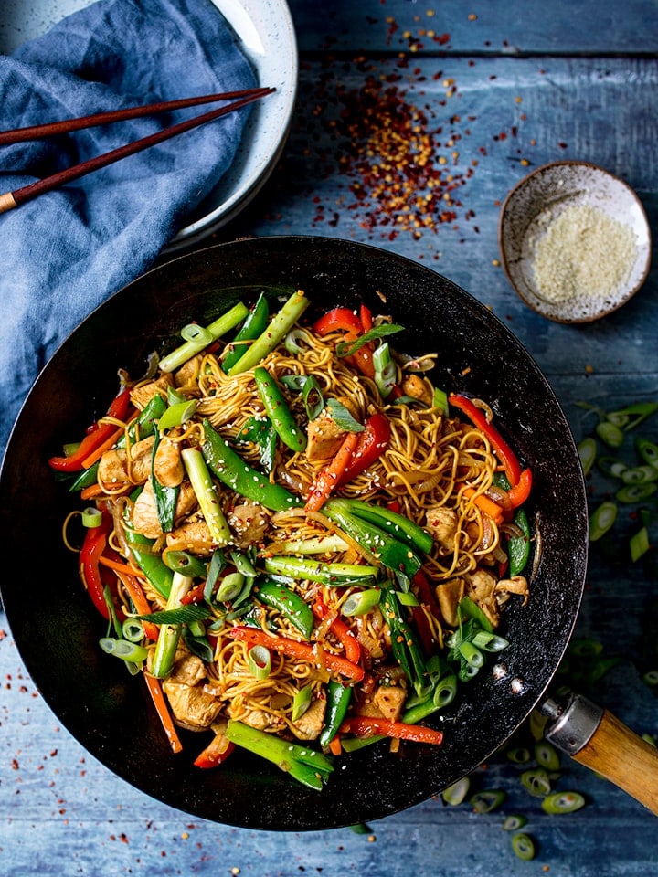 chicken lo mein in a wok on a blue background