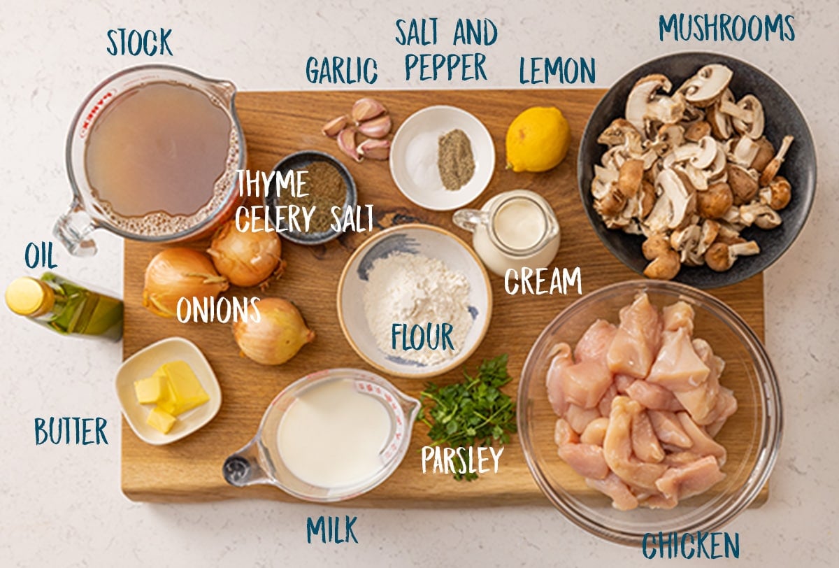 Ingredients for creamy chicken and mushroom casserole on a wooden chopping board against a light background.