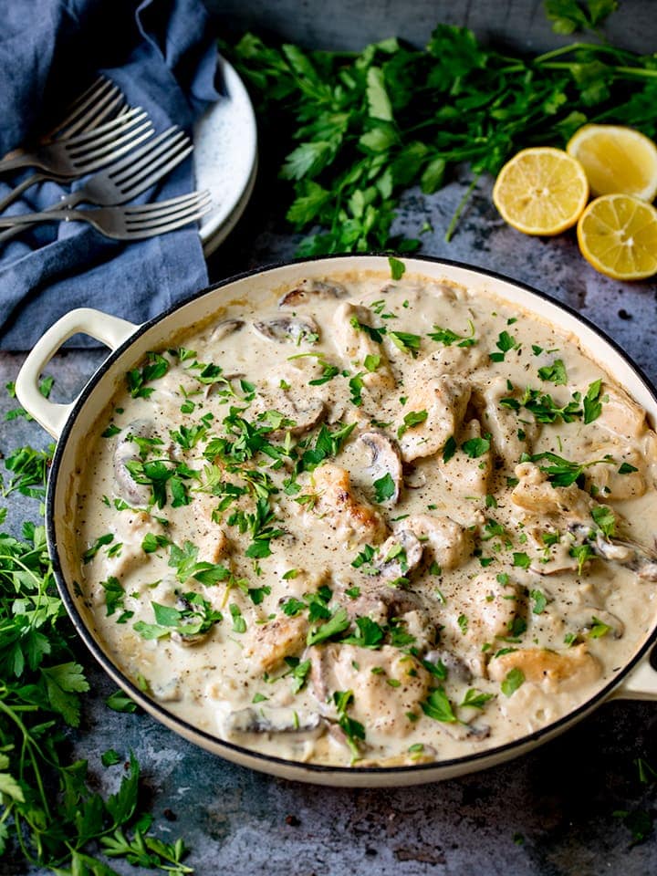 Overhead photo of Creamy Chicken and Mushroom One Pan Casserole in a pan on a blue background. Parsley and lemon scattered around the pan,