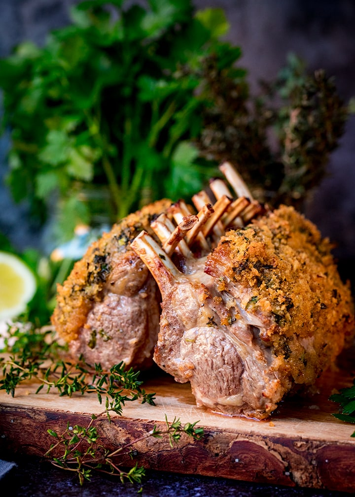 two herb-crusted racks of lamb on a wooden board