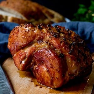Square image of a baked ham join with honey mustard glaze on wooden board