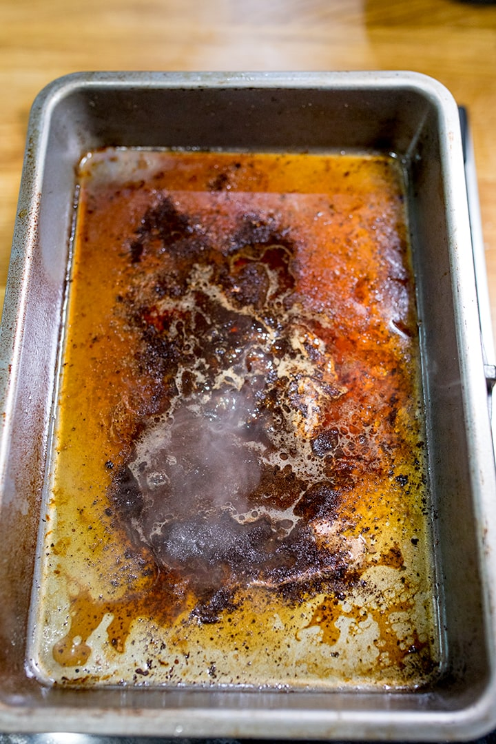 Heating meat juices and crumbled stock cube for gravy in a roasting tin
