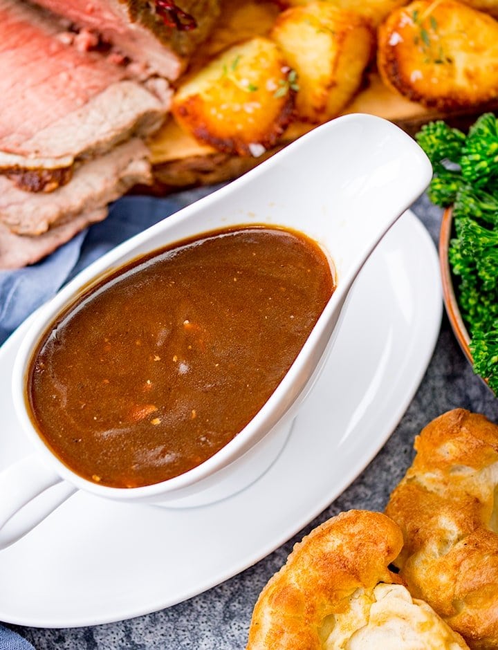 Beef gravy in white jug surrounded by beef and potatoes