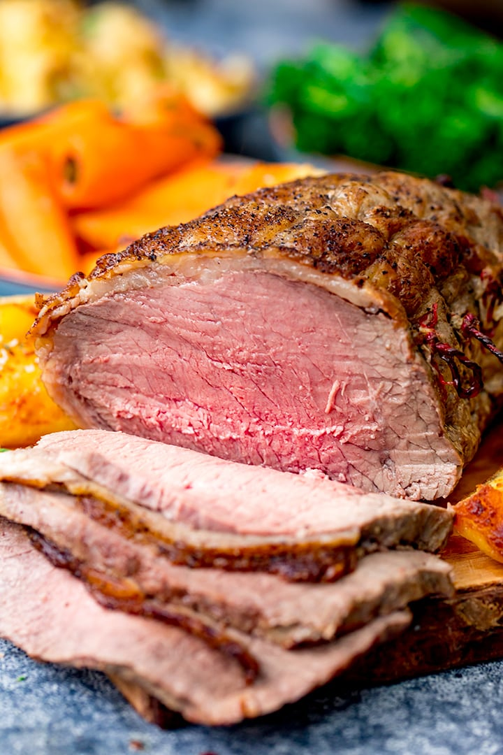 Tall image of Roast beef on a board with roast potatoes