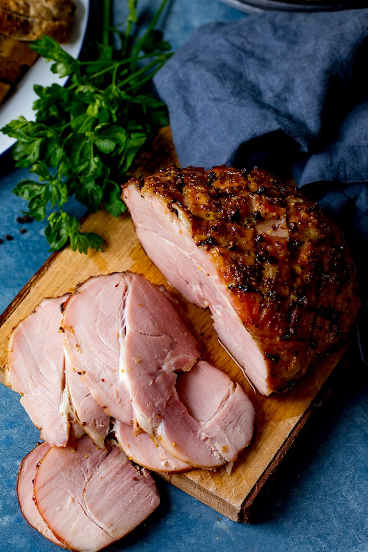 Overhead image of honey and mustard glazed baked ham on a wooden board with slices taken