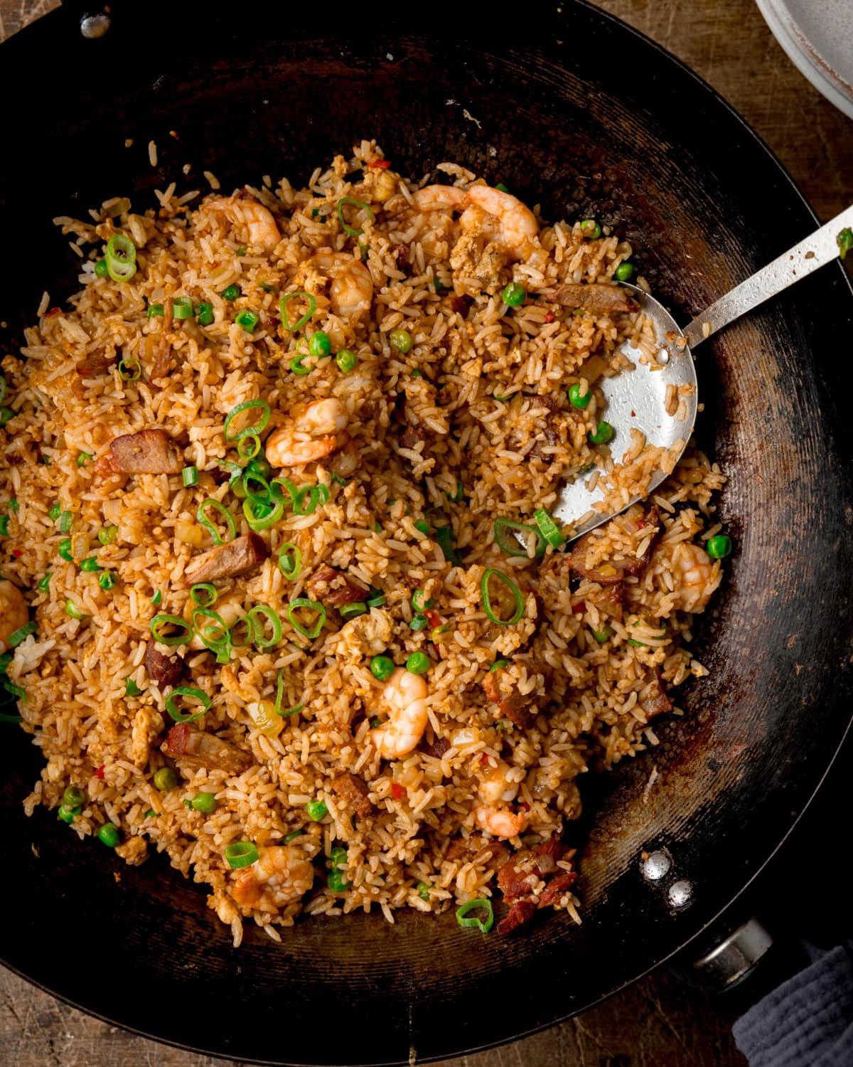 Yeung Chow Fried Rice with spring onions and peas in a wok with a metal spatula digging in.