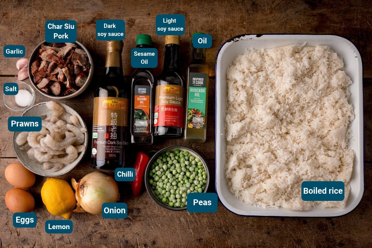 Ingredients for easy Yeung Chow Fried Rice, including char siu pork, prawns, boiled rice, eggs, lemon, onion, chilli, peas, garlic, salt, soy sauces, sesame oil, and avocado oil, labelled with their names.