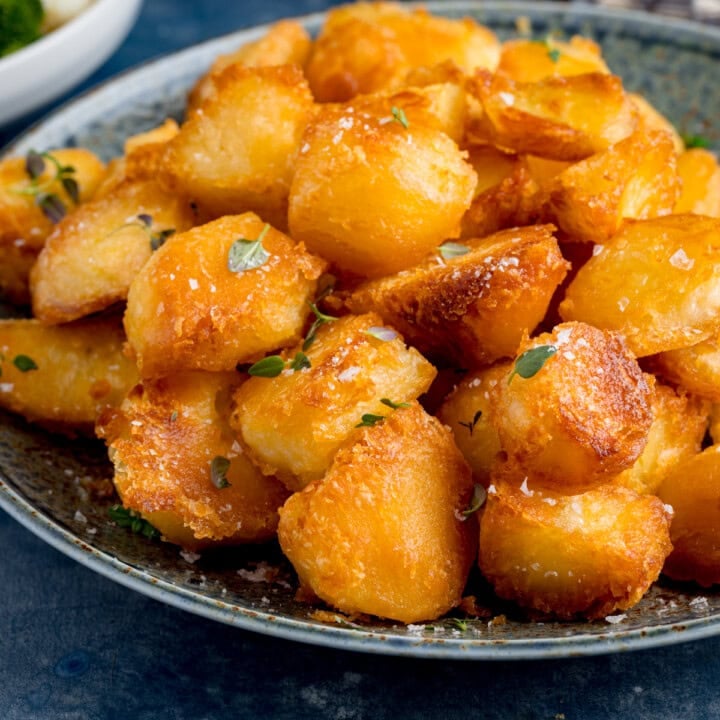 A plate of crispy roast potatoes garnished with fresh herbs and a sprinkle of salt. The roast potatoes are on a blue plate.