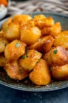 A plate of perfect roast potatoes, crispy and golden, garnished with thyme and a sprinkle of sea salt.