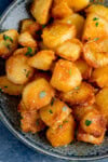 Overhead image of a plate of crispy roast potatoes, golden and perfectly seasoned, garnished with coarse salt and fresh herbs.